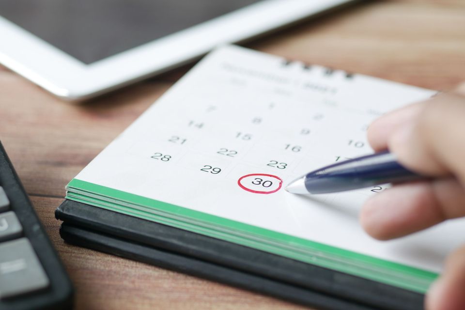 Hand circling a date on a paper calendar with a pen